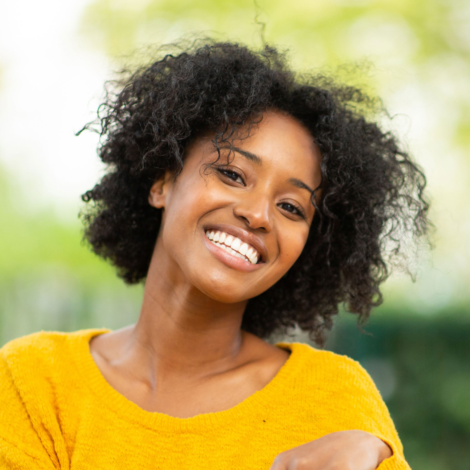 african american woman wearing yellow sweater sitting outside smiling at camera