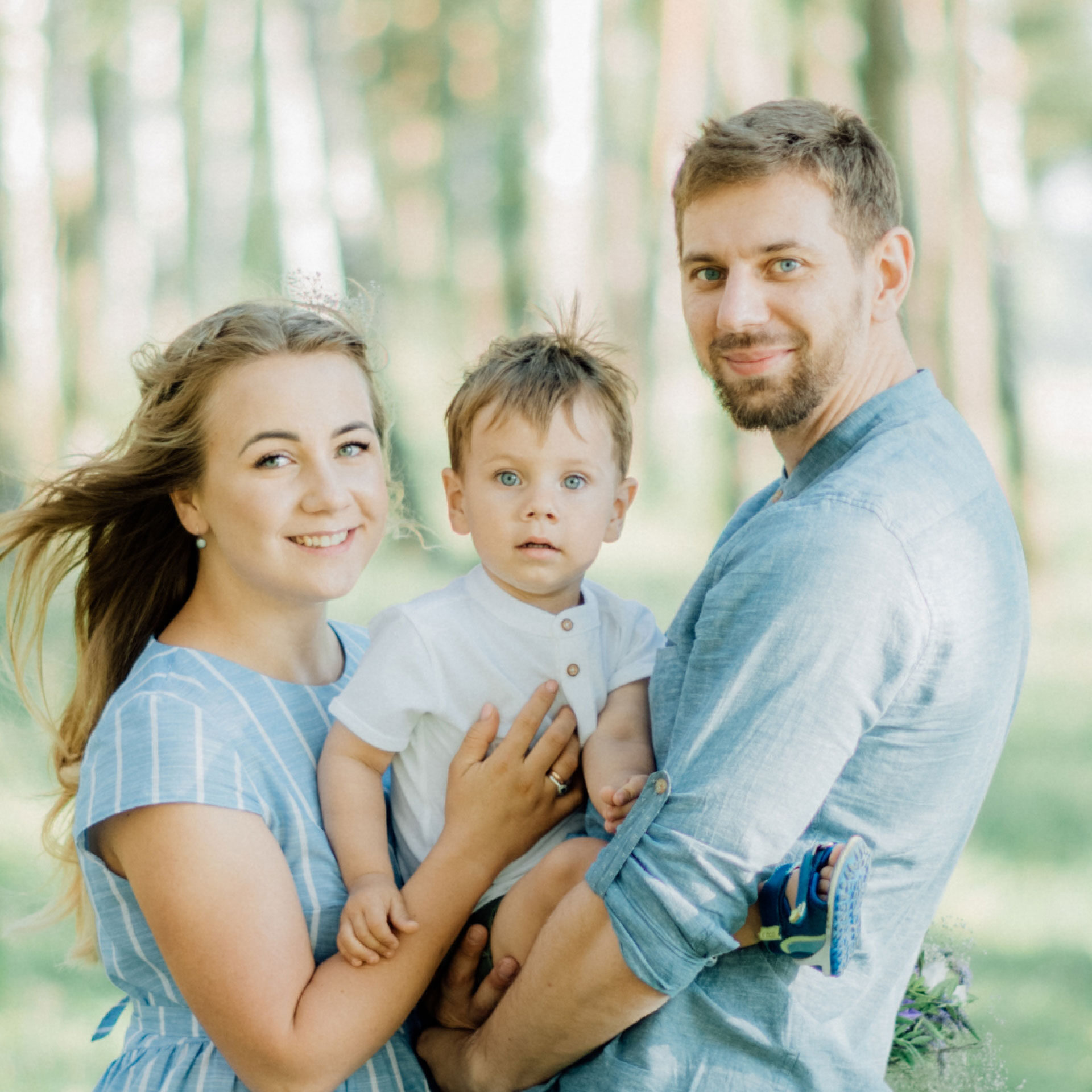 young couple with toddler son smiling at camera while outside