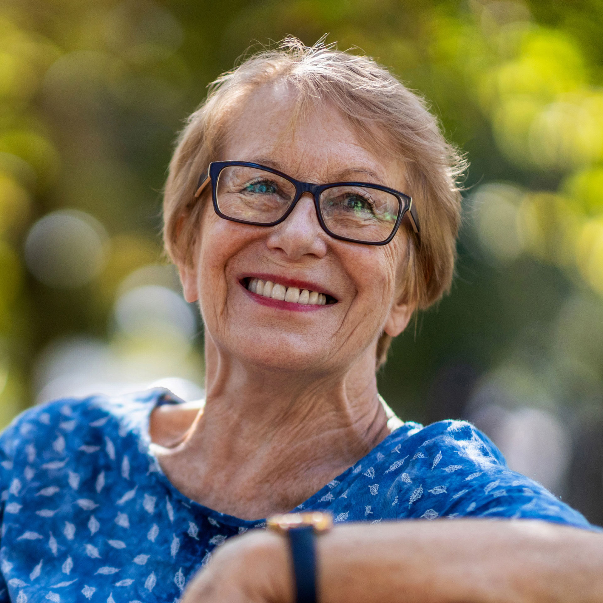older woman wearing glasses sitting outside smiling and looking to the right
